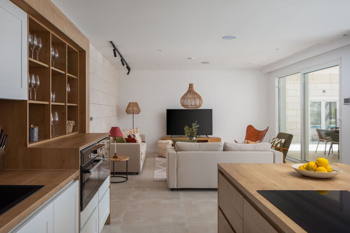Een moderne keuken met inbouwmeubels, een eethoek met tafel en stoelen, een bank en een televisie op de achtergrond.