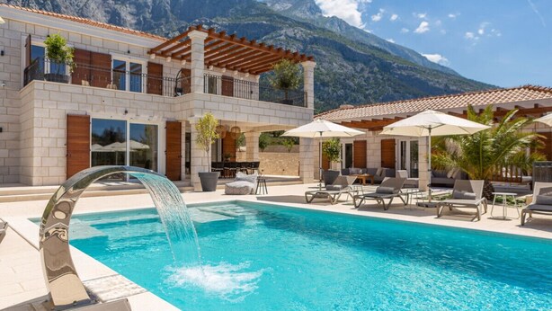 A pool with a waterfall feature, lounge chairs, and a mountain backdrop. - Villa Vespera (Makarska)