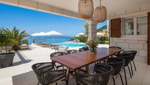 A patio with a wooden table and chairs, a pool, and a view of the sea. - Villa Vespera (Makarska)