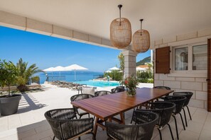 Eine Terrasse mit Holztisch und -stühlen, ein Pool und Meerblick.