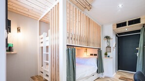 Ein kleines Zimmer mit Etagenbett, Schreibtisch, Heizkörper und einer Tür mit Vorhang.