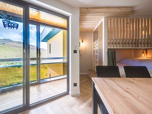 Ein modernes Schlafzimmer mit einem großen Schiebeglasfenster, das auf einen Balkon führt, einer Holzbodenverkleidung und einem Bett mit Kopfteil.