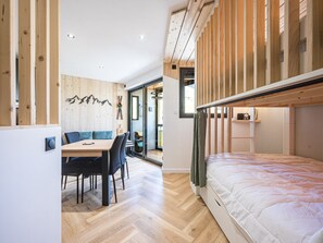 Ein gemütlicher Raum mit Etagenbett, einer Essecke mit Tisch und Stühlen sowie einer Holzwand mit Bergdeko.