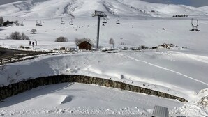 Ein mit Schnee bedeckter Ski-Hang mit einer Holzhütte, einer Steinmauer und einer Seilbahn im Hintergrund.