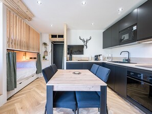 A modern kitchen with a dining table, built-in appliances, and a mounted television. - Studio with slope view - 5 guests (La Toussuire)
