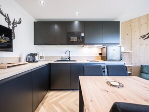 Eine moderne Küche mit dunklen Schränken, einem Holztisch und einem wandmontierten Flachbildfernseher.