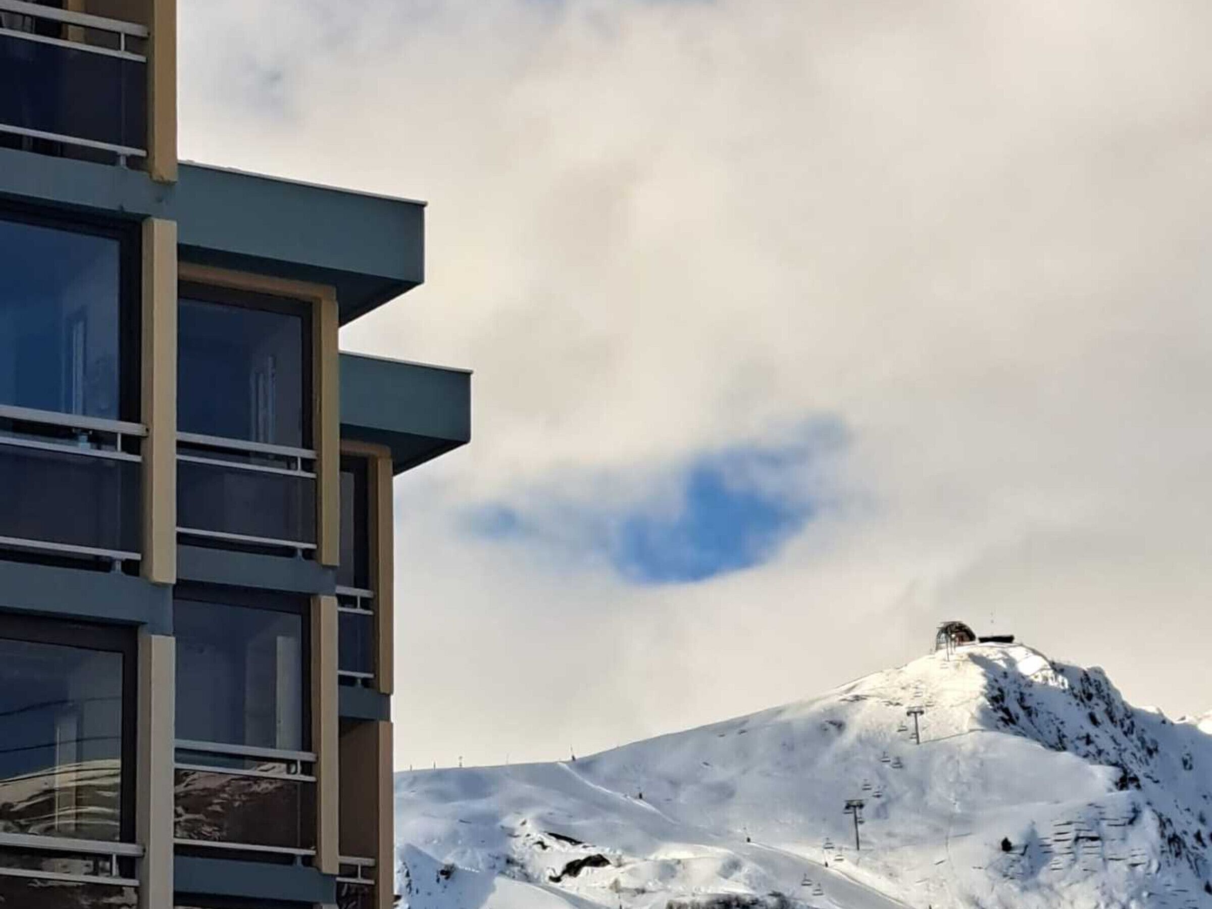 Een modern gebouw met meerdere verdiepingen en grote ramen, met een besneeuwde berg op de achtergrond en een heldere lucht.