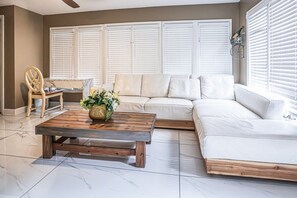 A living room with a sectional sofa, a wooden coffee table with a vase, a wooden chair, and a window with blinds. - Moss drive retreat - Close to the woods (Douglasville)