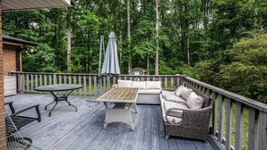 Um deck de madeira com mobiliário externo, incluindo uma mesa e um sofá, cercado por um corrimão de madeira.