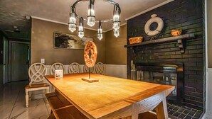 Uma sala de jantar com mesa de madeira, cadeiras, um candelabro, lareira e um quadro na parede.