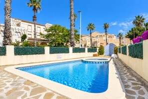 Une piscine bordée de pierres, entourée de palmiers et d’une haie.