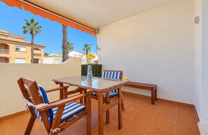 A balcony with a glass table and wooden chairs, a small vase with flowers, and a view of buildings and palm trees. - Apartamento Mediterraneo Javea Arenal, with AC and private pool (Javea)