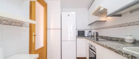 Una cocina compacta con armarios blancos, un refrigerador, un microondas, una cafetera y un lavamanos.