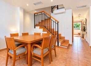 A dining area with a wooden table and chairs, a staircase with black railings, and an air conditioning unit on the wall. - Apartamento Mediterraneo Javea Arenal, with AC and private pool (Javea)
