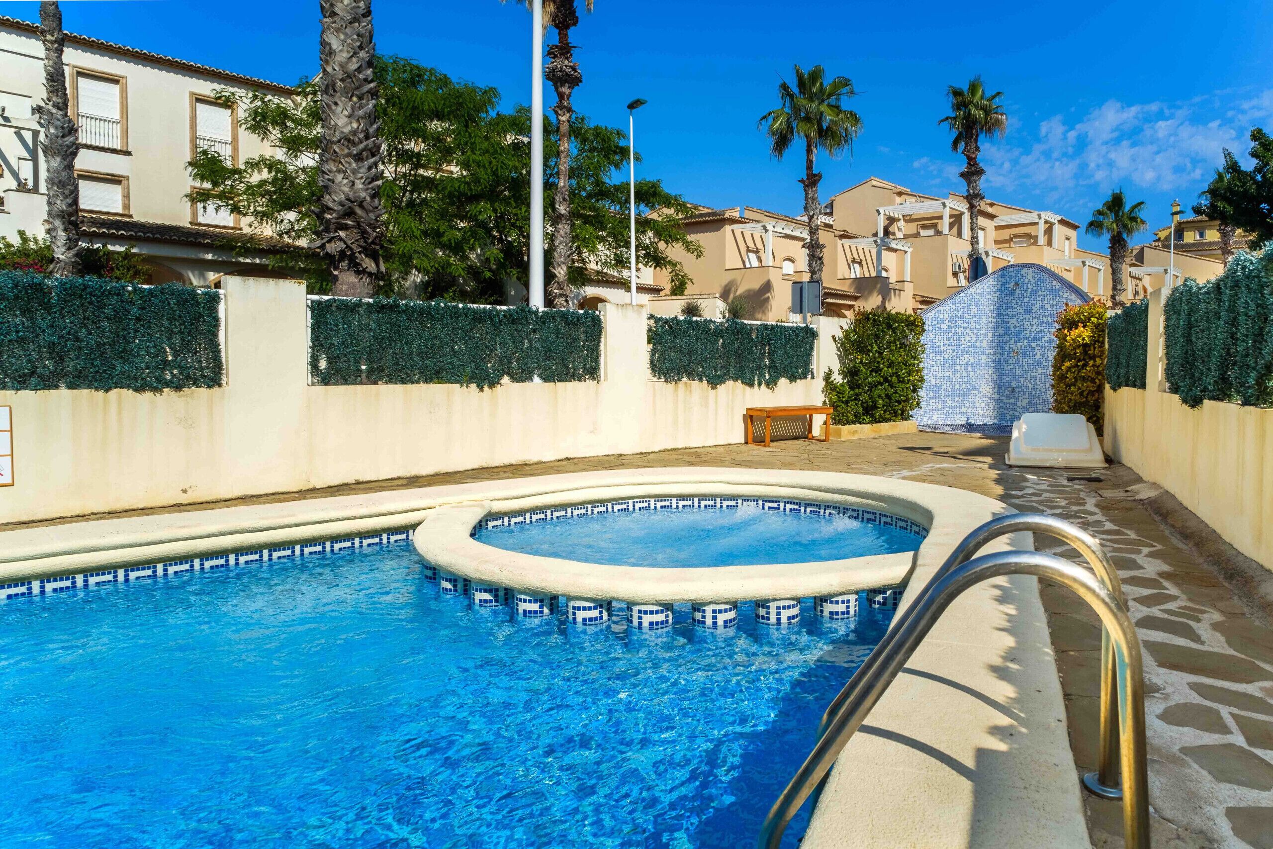 A swimming pool with a tiled edge, a metal handrail, and a stone-tiled deck.