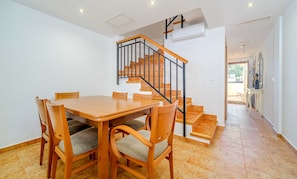 Ein Essbereich mit Holztisch und -stühlen, eine Treppe mit schwarzen Geländern und eine Klimaanlage an der Wand.