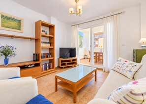 A living room with a television, bookshelves, a coffee table, and a sofa. - Apartamento Mediterraneo Javea Arenal, with AC and private pool (Javea)