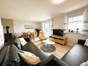 Ein modernes Wohnzimmer mit Sofa, Fernseher, Esstisch und Stühlen.