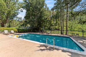 A rectangular swimming pool with a metal ladder, surrounded by a paved deck and a black metal fence. - Trailside Retreat Near Vail Village W/Pool (Vail)