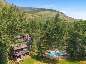 A multi-story building with a pool surrounded by trees, set in a hilly landscape. - Trailside Retreat Near Vail Village W/Pool (Vail)