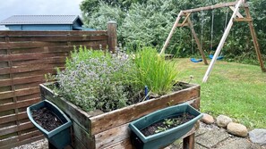 Ein erhöhter Blumenkasten mit Pflanzen, eine Holzschaukel und eine blaue Gartenhütte im Hinterhof.