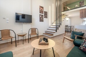 A modern living room with a flat-screen TV, wicker chairs, a round coffee table, a staircase, and a sofa with cushions. - Echo City Loft by Rentals Pro - Nea Moudania Halkidiki (Nea Moudania)