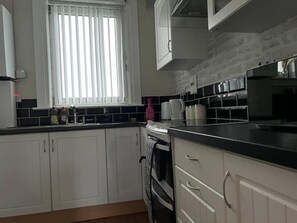 A kitchen with white cabinets, a black countertop, a window with blinds, and a tiled backsplash. - 3 Bedroom Flat - Sleeps 6 - Free Parking (Kirkcaldy)