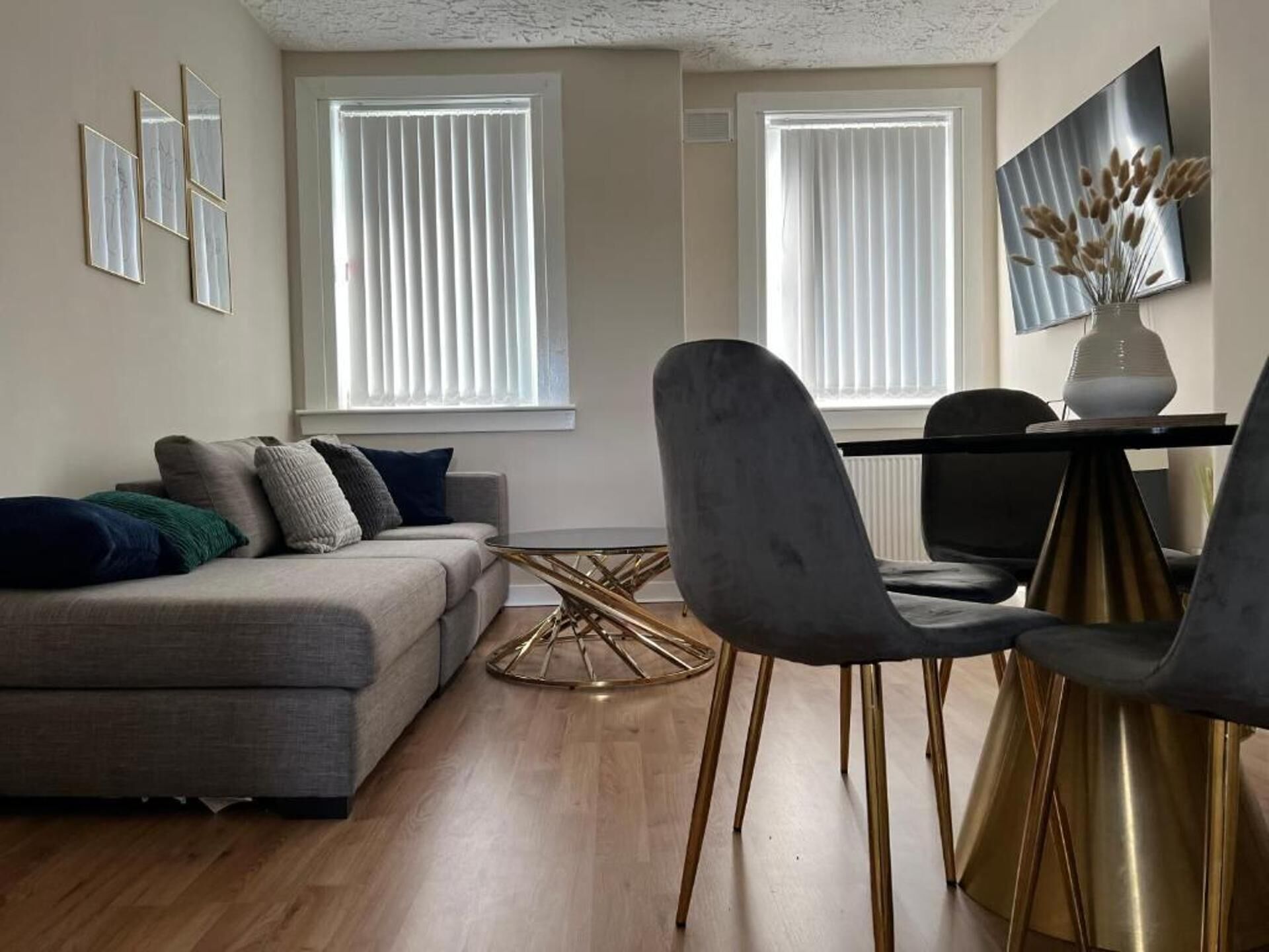 Uma sala de estar moderna com um sofá cinzento, uma mesa de centro redonda e duas cadeiras com pés dourados.