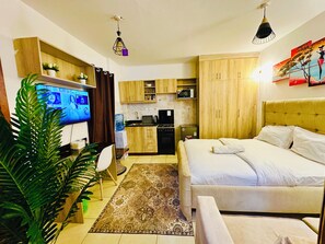 Habitación de hotel pequeña con cama, kitchenette, televisor y comedor.