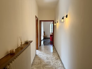 Ein Flur mit Heizkörper, einem Holzbodenregal mit Dekoration, einem Marmorboden und einer Tür zu einem weiteren Zimmer.