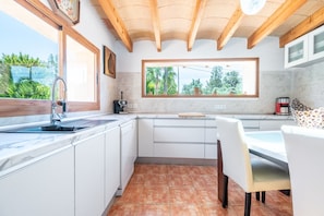 A kitchen with a window, white cabinets, a sink, and a dining area with chairs.