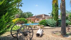 Um edifício rústico com piscina, rodeado por vegetação e um carrinho de madeira.