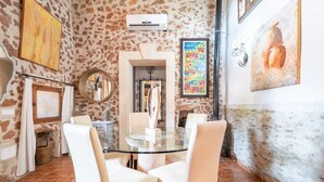 Uma área de refeições com mesa de vidro e cadeiras brancas, paredes de pedra e obras de arte.