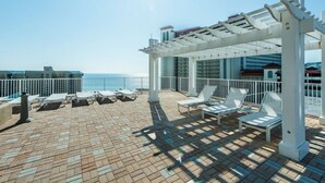 En takterrass med solstolar, en pergola och utsikt över havet.