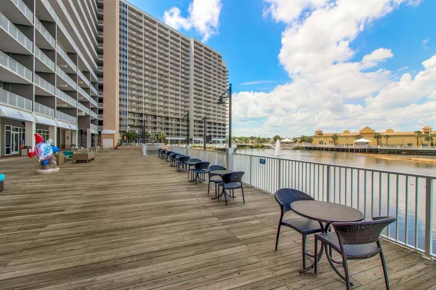 A hotel deck with outdoor seating, a view of a water body, and a large building in the background.