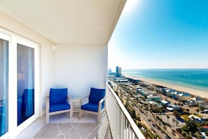 Ein Balkon mit zwei blauen Stühlen, einem kleinen Tisch und Blick auf Strand und Stadtlandschaft.
