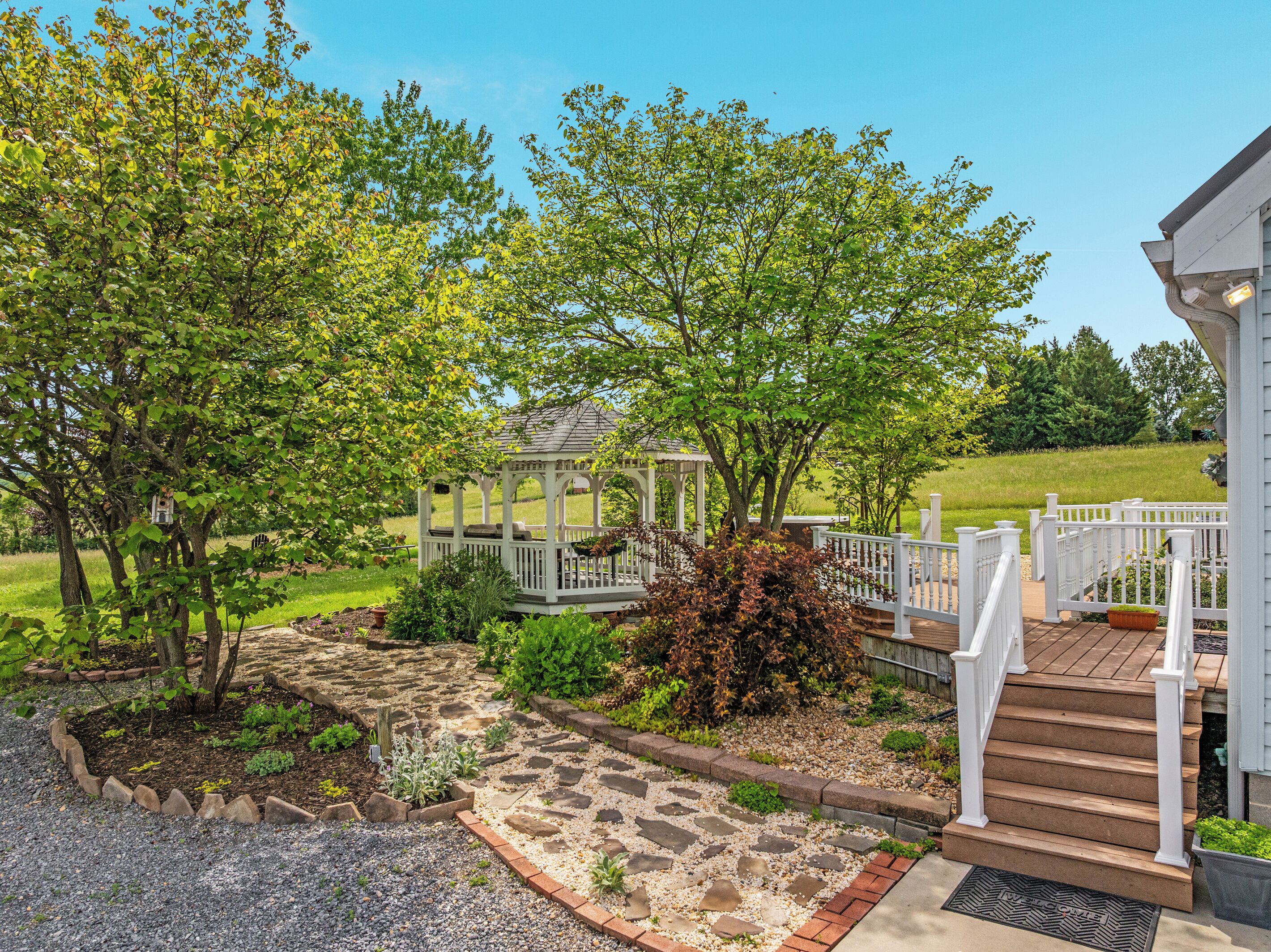A garden with a gazebo, stone pathway, and a wooden deck with steps.