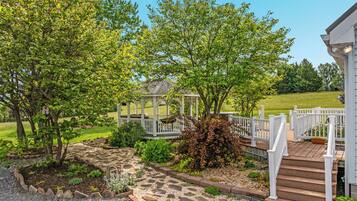 A garden with a gazebo, stone pathway, and a wooden deck with steps.