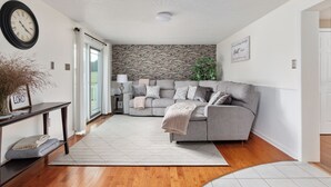A modern living room with a grey sofa, a wooden floor, a white ceiling, and a brick wall.