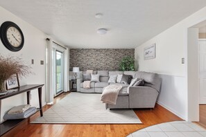Un salon moderne avec un canapé gris, un plancher en bois, un plafond blanc et un mur en briques.