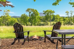 Deux fauteuils Adirondack sont placés face à un feu de camp, avec un champ herbeux et des arbres en arrière-plan.