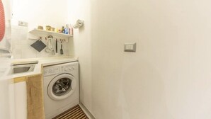 A compact laundry area with a washing machine, a drying rack, and a shelf with toiletries. - Delightful little house to discover the truest and most popular Rome in the heart of Pigneto (Roma RM)