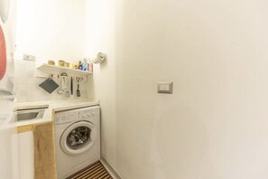 A compact laundry area with a washing machine, a drying rack, and a shelf with toiletries. - Delightful little house to discover the truest and most popular Rome in the heart of Pigneto (Roma RM)