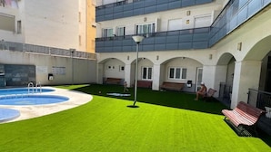 Un patio con piscina, césped artificial, bancos y una farola.