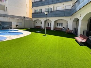 A courtyard with a swimming pool, artificial grass, benches, and a lamp post. - Apartment very close to the beach and the subway station. (El Campello)