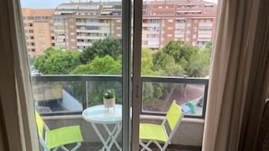 Un balcón con una mesa y dos sillas, con vista a una zona residencial con edificios y zonas verdes.