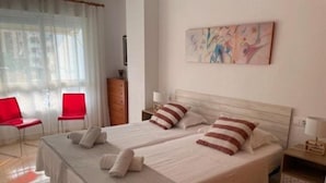 Habitación doble con dos camas, un aparador de madera, una silla roja y un cuadro en la pared.