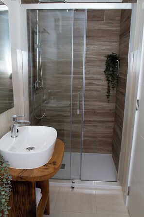 A modern bathroom with a glass-enclosed shower, a wooden vanity, and a mirror.