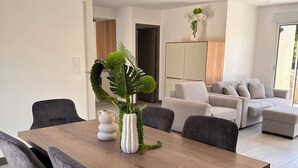 Ein moderner Essbereich mit einem Holztisch, grau gepolsterten Stühlen und einer dekorativen Pflanzengruppe als Mittelstück.