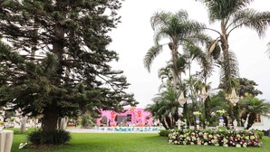 A stage with a pink backdrop, surrounded by palm trees and a flower arrangement. - w Spacious 12br Stay w Pool BBQ in Pachacamac (Pachacámac)